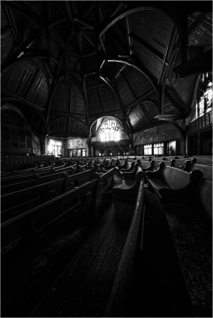 A dimly lit space with wooden pews and an elaborate ceiling, exuding a cozy solemnity.