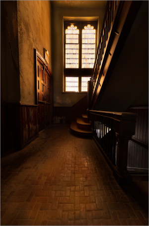 A dimly lit staircase with ornate windows casting soft light; a scene of quiet reflection.