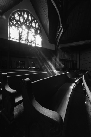 A sunbeam graces the empty pews beneath a stained glass window.