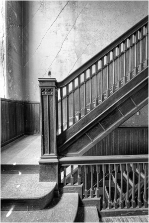A shadowy staircase with intricate woodwork and a foreboding ambiance.