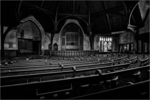 A dark, abandoned church interior with wooden pews and a vaulted ceiling.