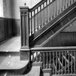 A dark wooden staircase with peeling paint, shadows pooling in corners.