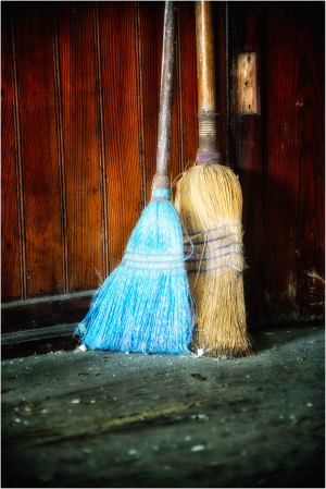 Two ominous brooms stand sentinel against a weathered wooden backdrop.
