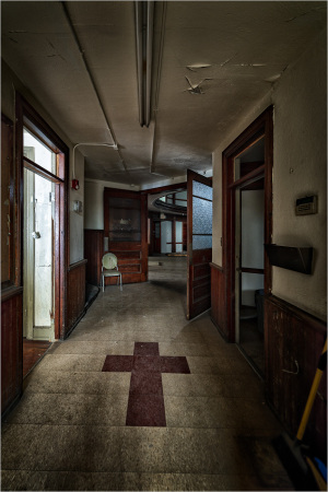 A corridor featuring wooden doors and tile flooring with a cross symbol on the ground.