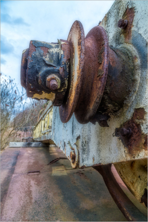Close-up of a rusted trolley wheel, nature reclaiming metal remnants.