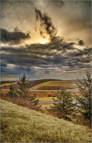 A dramatic sky over rolling hills and trees, hinting at nature's mood swings.