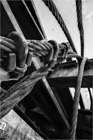 Close-up of thick, weathered ropes intertwined with metal, casting shadows in stark black and white.