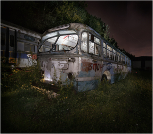 An abandoned, decaying bus shrouded in darkness and overgrown foliage.