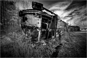 A forsaken trolley, rusted and overgrown, looms in a desolate graveyard of forgotten machinery.