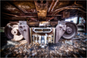 Rusting wheels of an ancient trolley, entwined in shadows and decay, evoke a sense of forgotten dread.