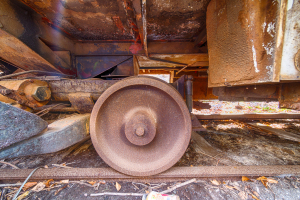 A rusted wheel of an ancient trolley lies amidst the shadows of forgotten machinery.