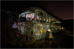 An abandoned, dilapidated bus looms in a desolate graveyard of forsaken vehicles.