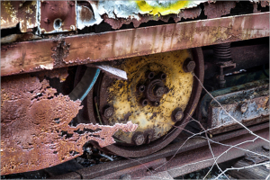 Close-up of a rusty wheel and machinery parts with peeling paint and cobwebs.
