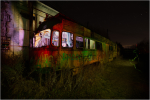 An abandoned trolley, shrouded in shadows, looms amidst encroaching darkness and wild overgrowth.