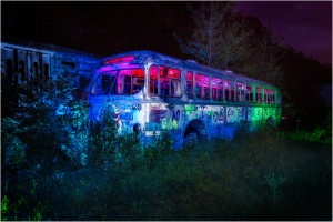 Abandoned trolley bus illuminated by colorful lights in a natural setting.