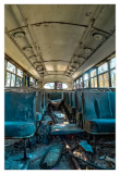 Interior of an abandoned trolley bus with worn seats and debris on the floor.