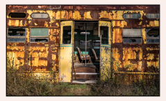 A rusty, abandoned trolley car with peeling yellow paint and overgrown weeds.