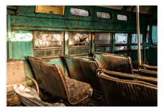 Interior of an abandoned trolley, faded green seats, dust and decay linger in the air.