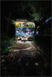 An abandoned, graffiti-covered trolley looms in an overgrown graveyard of forgotten transit.