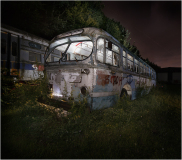An abandoned, decaying bus shrouded in darkness and overgrown foliage.