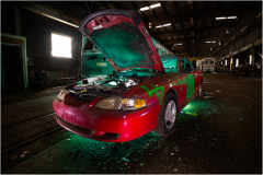 A forsaken vehicle, its hood ajar, bathed in an eerie green glow amidst the shadows of decay.