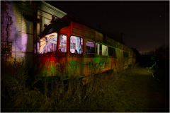 An abandoned trolley, shrouded in shadows, looms amidst encroaching darkness and wild overgrowth.