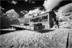 An abandoned industrial building with overgrown grass and a decaying loading dock.
