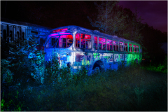 Abandoned trolley bus illuminated by colorful lights in a natural setting.