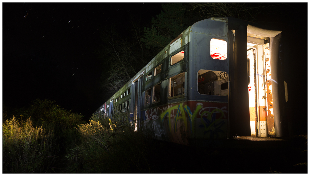 Abandoned train car illuminated at night, surrounded by tall grass.