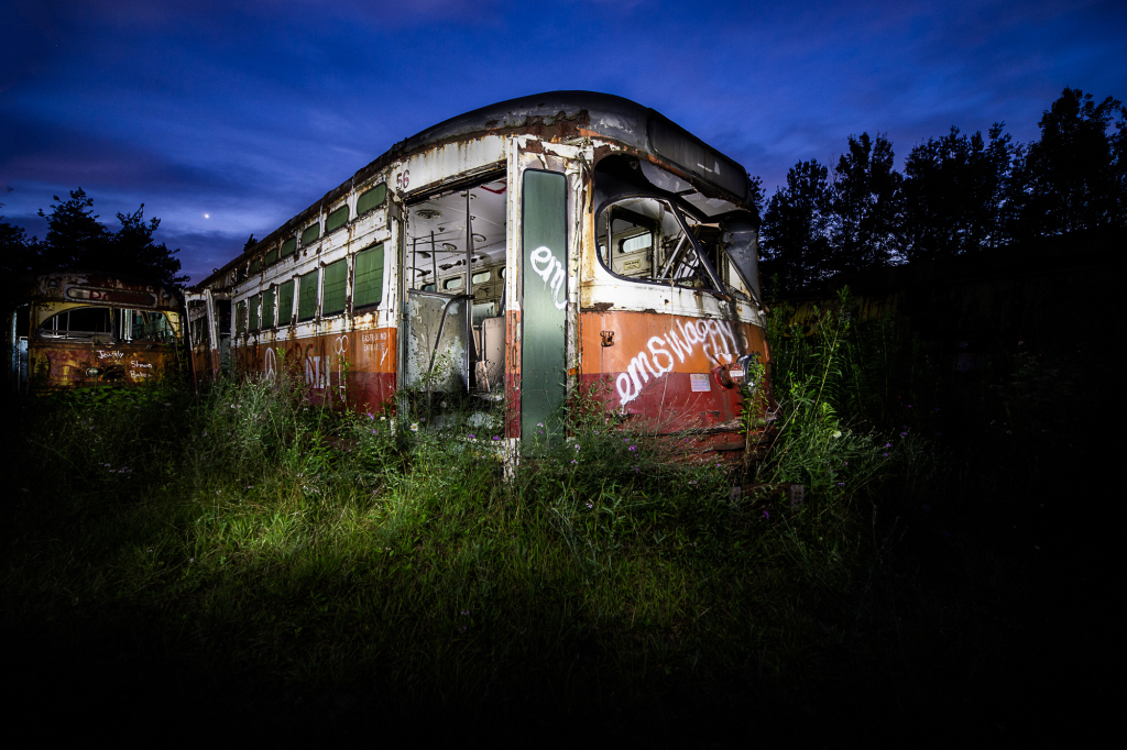 An abandoned trolley car, rusting in the shadows, overgrown with wild grass.
