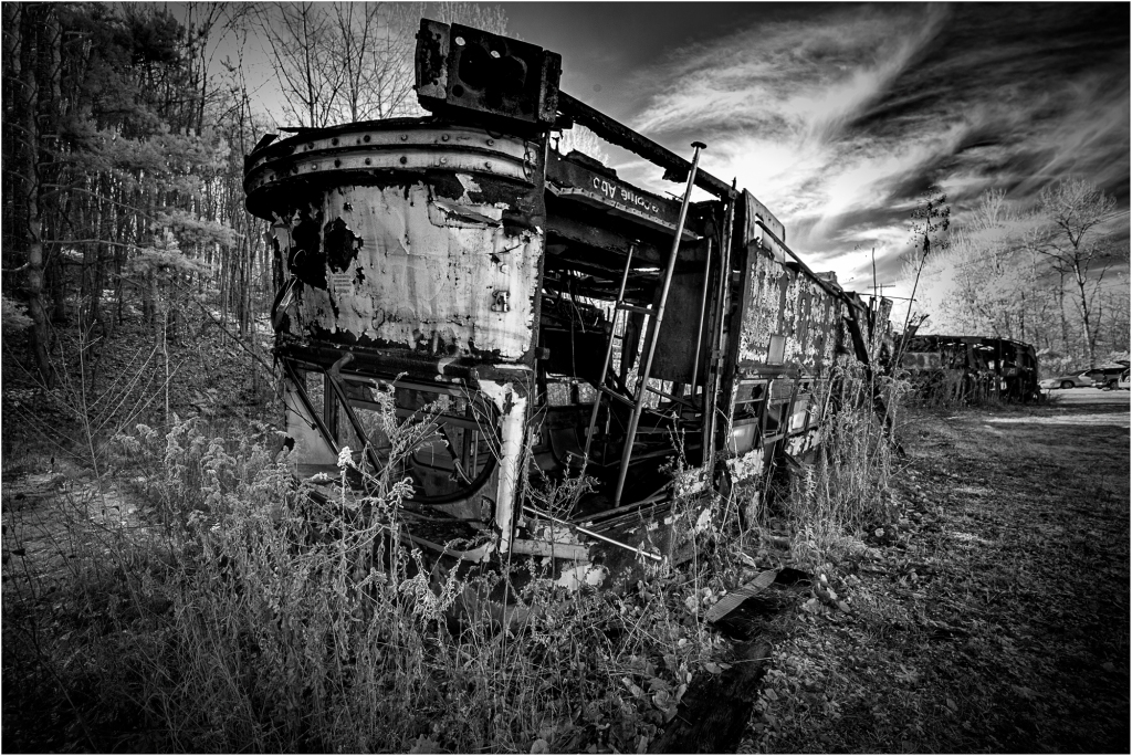 A forsaken trolley, rusted and overgrown, looms in a desolate graveyard of forgotten machinery.