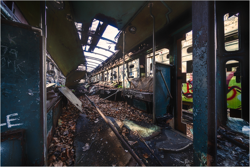 An abandoned trolley interior, cloaked in decay and shadows, whispers of forgotten journeys.