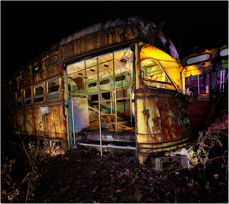 An abandoned trolley, rusted and peeling, looms in the shadows of a graveyard.