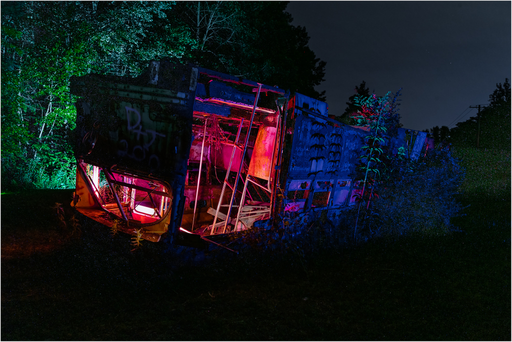 Abandoned trolley in a graveyard, illuminated by colorful lights.