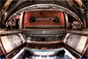 Interior of a decaying theater, with a wide view of an empty stage and ornate ceiling details.