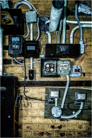 Wires and electrical panels on a weathered brick wall, tangled and raw.
