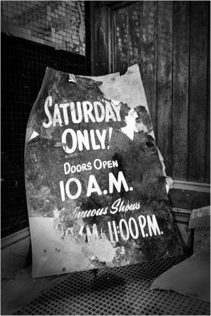 Faded sign announcing Saturday showtimes, an echo of forgotten revelries.