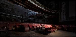 Interior of an abandoned theater with worn red seats and peeling walls, dimly lit