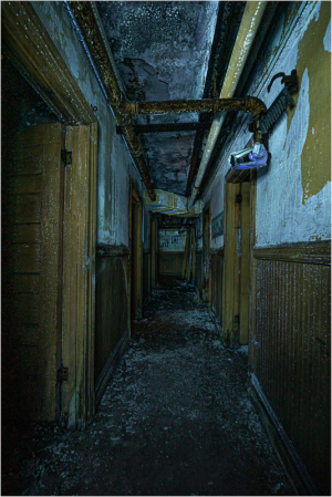 Dark, abandoned corridor with peeling walls and exposed pipes.