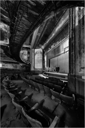 Interior view of an abandoned theater featuring worn seats and a faded stage.