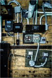 Wires and electrical panels on a weathered brick wall, tangled and raw.