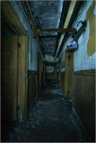 Dark, abandoned corridor with peeling walls and exposed pipes.