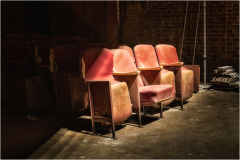 Empty, worn theater seats bathed in dim light, shadows lurking in the corners.