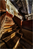 A dilapidated staircase in an abandoned theater, shadows dance upon the wooden steps.