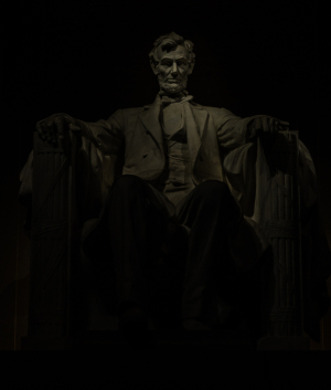 A statue of Abraham Lincoln seated in deep shadow, solemn and majestic.
