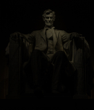 A statue of Abraham Lincoln seated in deep shadow, solemn and majestic.