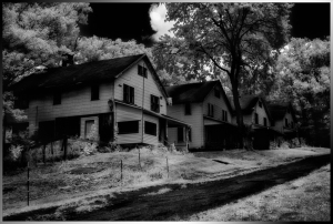 Black and white photo of abandoned houses lined along a dirt path.