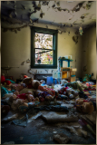 A cluttered, abandoned room filled with toys and peeling walls.